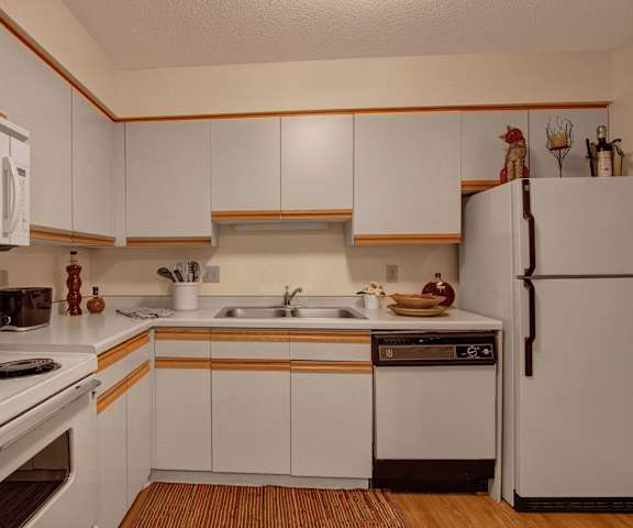 A spacious kitchen with white appliances, overhead lighting, light countertops with lots of room, a bar counter with barstools, and large wooden cabinets at Town Centre Apartment Homes. 
