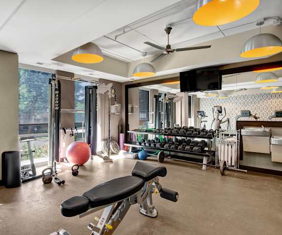 A spacious gym with cardio machines, windows, TVs, and weights at Vue Apartment Homes. 