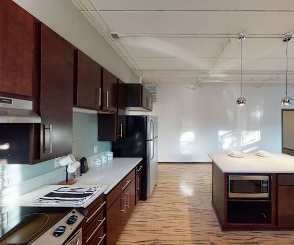A large kitchen with stainless steel appliances, a kitchen island, white marble countertops, and large, dark wooden cabinets at Vue Apartment Homes. 