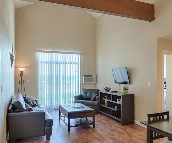 The living room with a couch, coffee table, decorations, a TV, and balcony at Dakota Ridge Apartments. 