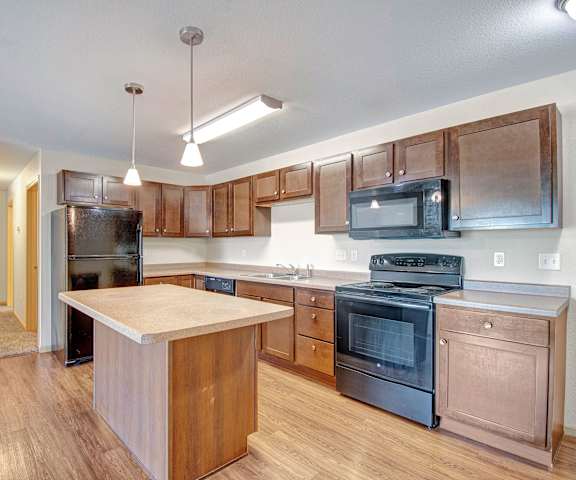 A large kitchen with black appliances, spacious marble countertops, and large wooden cabinets with decorations at Pheasant Ridge Apartments. 