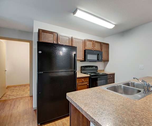 A large kitchen with black appliances, spacious marble countertops, and large wooden cabinets with decorations at Pheasant Ridge Apartments. 