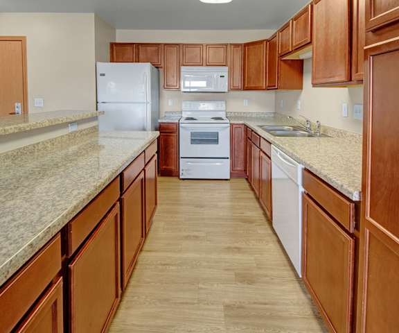 A large kitchen with white appliances, a light counter with lots of room, and spacious wooden cabinets at Pheasant Ridge Apartments. 