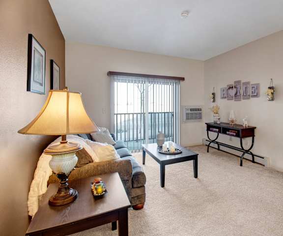 The living room with a couch, coffee table, decorations, wall art, and a balcony at Prairie Pines at the Ridge Apartment Homes. 
