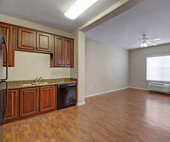 An empty living room with hardwood flooring and kitchen with a large window and ceiling fan at Prairie Vista Apartment Homes. 