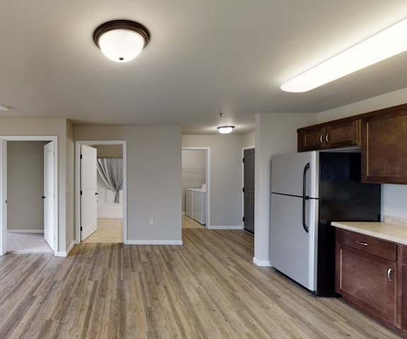 An empty living room with hardwood flooring and kitchen with stainless steel appliances, large dark wood cabinets, and doors to other rooms at Renaissance Heights Apartment Homes. 