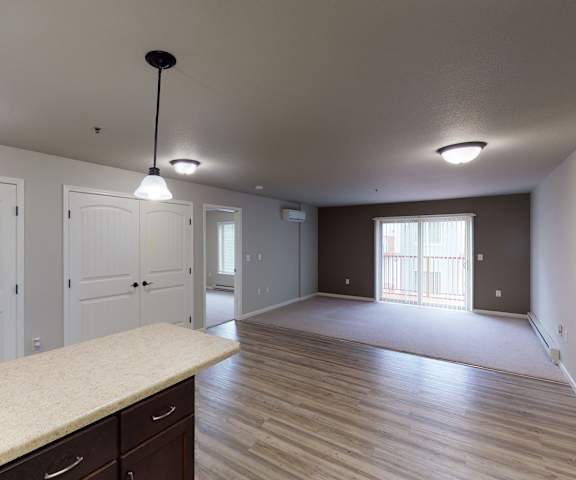 A view of the empty carpeted living room with a balcony and the kitchen at Renaissance Heights Apartment Homes. 