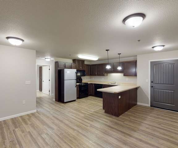 A large kitchen with stainless steel appliances, spacious marble countertops, and large wooden cabinets with the front door at Renaissance Heights Apartment Homes. 