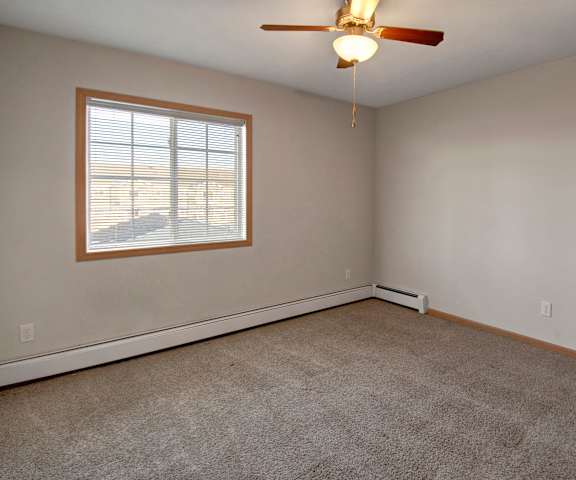 A large, empty carpeted bedroom with overhead lighting and a fan and a window at Roosevelt East Apartment Homes. 