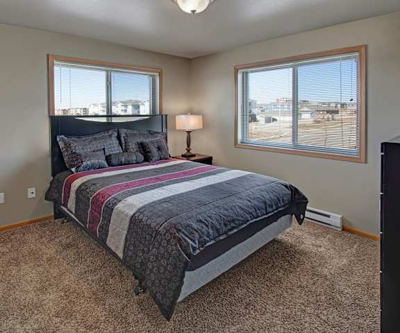 A spacious bedroom with a queen-size bed, a dresser, wall art, lamps, decorations, window, and nightstands at Vue 28 Apartment Homes. 