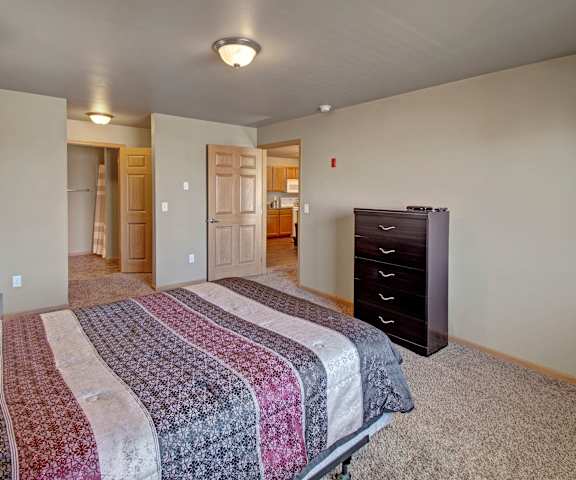 A spacious bedroom with a queen-size bed, a dresser, wall art, lamps, decorations, closet, and nightstands at Vue 28 Apartment Homes. 