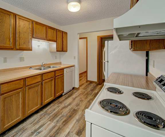 A spacious kitchen with white appliances, light counter, overhead lighting, and large wooden cabinets at Windscape Apartment Homes. 
