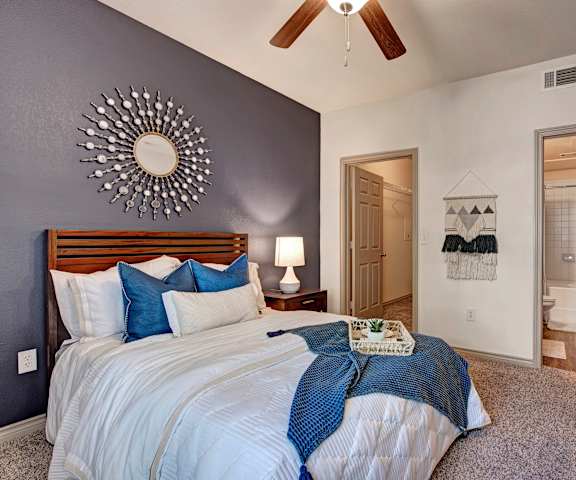 A bedroom with a large bed with a white and blue bedspread, a ceiling fan, and a bathroom attached at Aviare Arts District Apartments