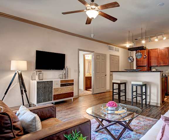 An open living room with couches, a coffee table, and a TV, and kitchen with a ceiling fan at Aviare Arts District