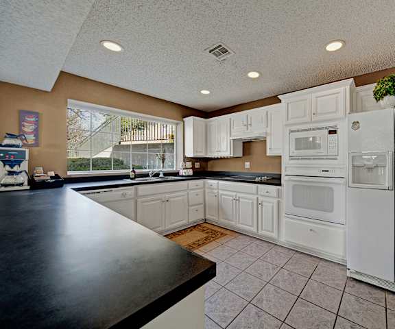 An updated kitchen with white appliances and black counter tops at Brookwood Village Apartments. 