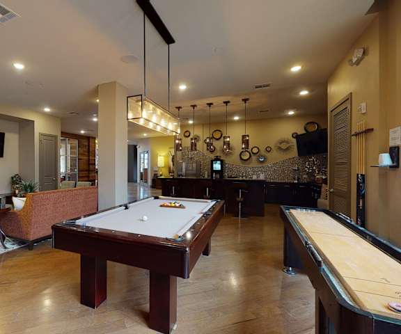 A wonderful resident lounge with tables, chairs, a pool table, a shuffleboard, two couches and a TV, with wall art and unique lighting in the background at Edge at Midtown Apartment Homes. 