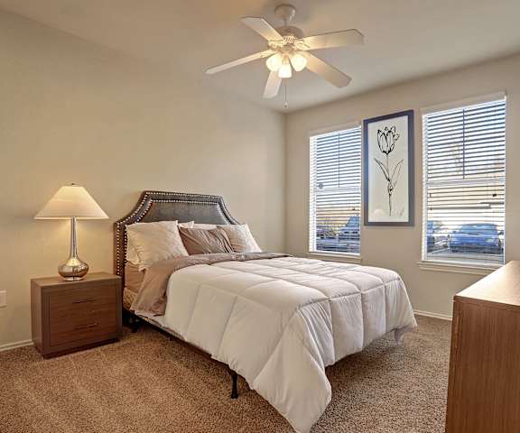 A bedroom with a queen-size bed, a dresser, decorations, windows, and nightstands at Memorial Creek Apartments. 