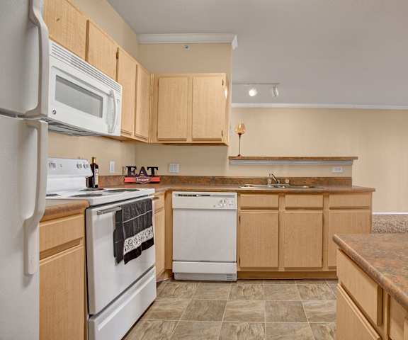 A large kitchen with white appliances, light counter with ample space, and spacious wooden cabinets at Memorial Creek Apartments