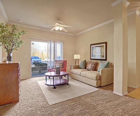 The living room with a couch, plush chairs, coffee table, decorations, a TV, and patio at Memorial Creek Apartments. 