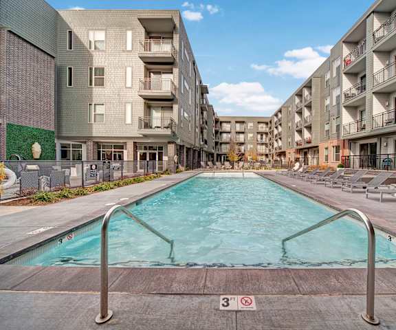 The turquoise outdoor pool with pool chairs, tables, and chairs with the apartments in the background at Metropolitan Apartments. 