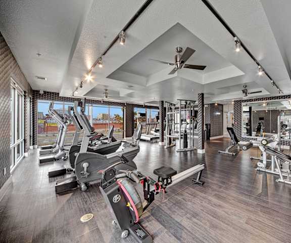 A gym with cardio machines, windows, TVs, and weights at Metropolitan Apartments. 