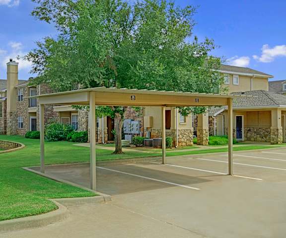 The covered parking surrounded by grass and trees right next to the apartment buildings at Quail Landing Apartment Homes. 