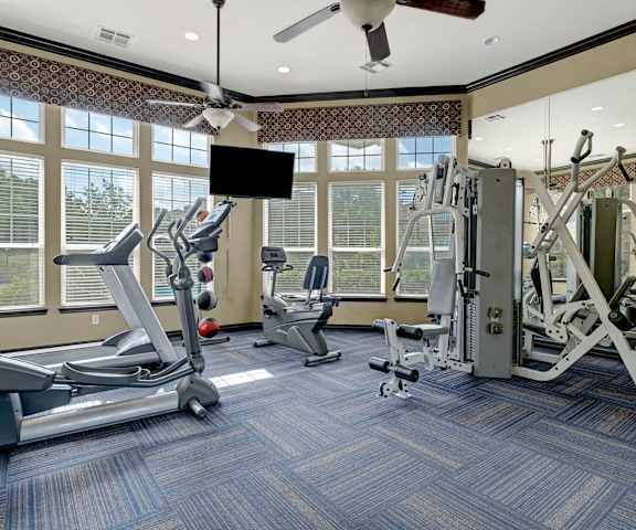 A gym with cardio machines, windows, TVs, and weights at Quail Landing Apartment Homes. 