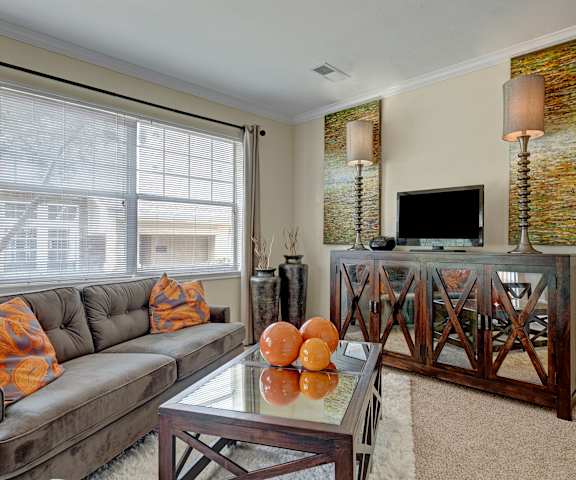The living room with a couch, plush chairs, coffee table, decorations, a TV, and windows at Quail Landing Apartment Homes. 