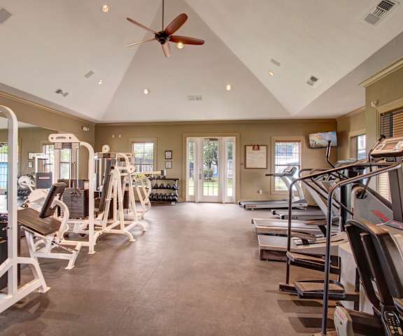 A spacious gym with cardio machines, windows, TVs, and weights at Woodland Park Apartment Homes. 