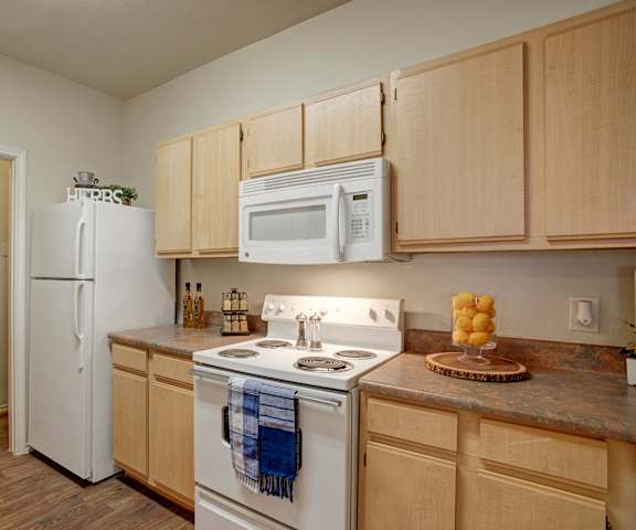 A cozy kitchen with white appliances, light counter, and spacious wooden cabinets at Woodland Park Apartment Homes.