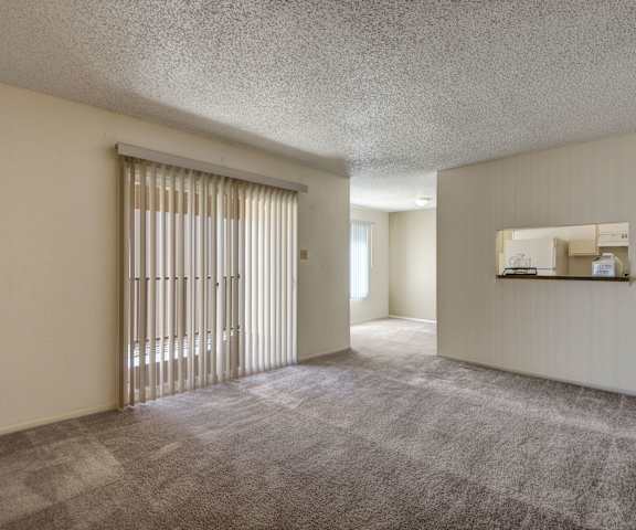 An empty living room with carpeting and a door to the balcony at Fairgreen. 