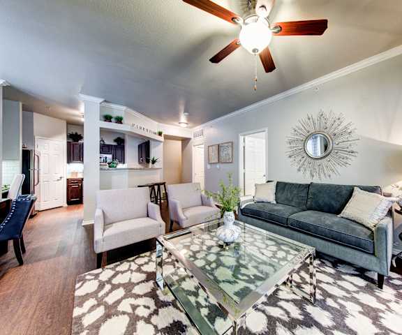 The living room with a couch, coffee table, decorations, a TV, and view of the kitchen at Firestone at West 7th. 