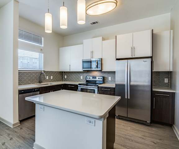 A kitchen with stainless steel appliances, marble countertops, and large black and white cabinets at Harmony Luxury Apartments. 