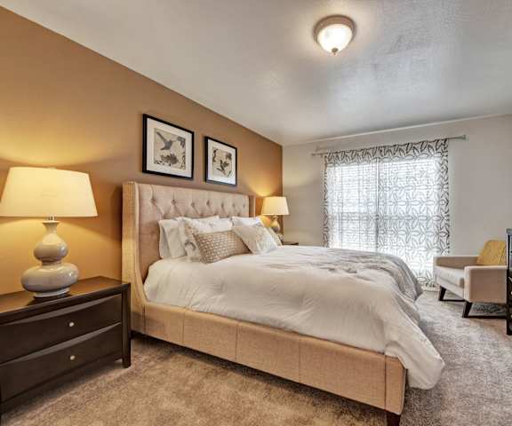 A bedroom with a queen-size bed, a dresser, decorations, window, and nightstands at High Plains Apartments. 