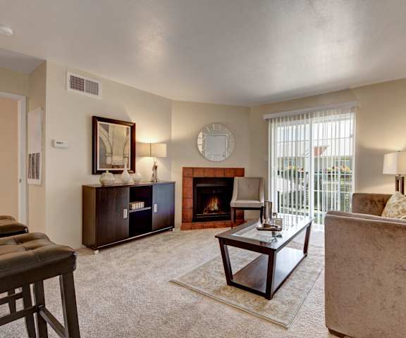 The living room with a couch, plush chairs, coffee table, fireplace, decorations, a TV, and balcony at High Plains Apartments. 
