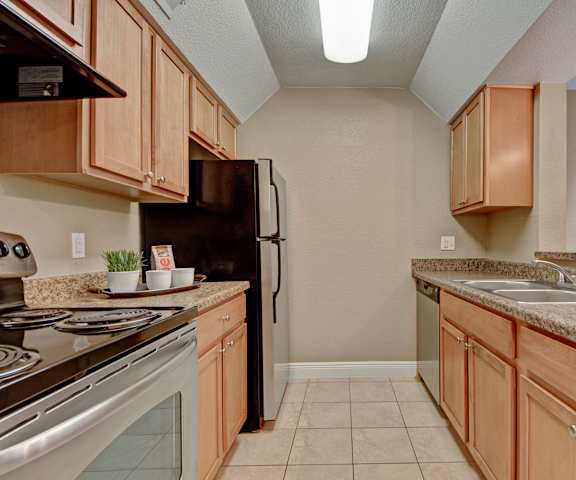 A kitchen with stainless steel appliances, marble countertops, and large wooden cabinets at Las Colinas Apartments. 