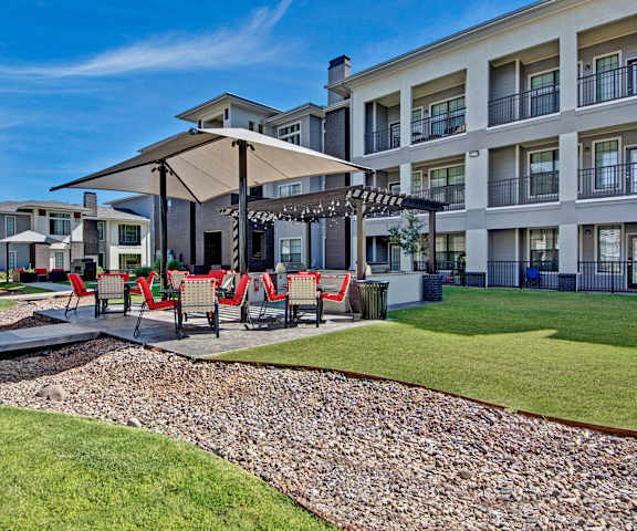 The outdoor patio with covered seating and tables, surrounded by grass and walkways at Le Mirage Apartments. 