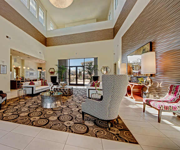 The leasing office with a desk and chairs as well as the resident lounge with couches, decorations, plush chairs, and coffee tables at Le Mirage Apartment Homes.