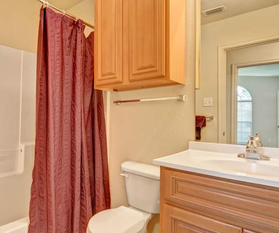 The bathroom with a sink, toilet, and shower with a red shower curtain and red towels at Lexington Court Apartment Homes. 