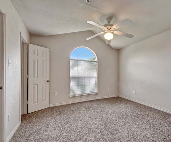 An empty carpeted bedroom with a window and a ceiling fan at Lexington Court Apartment Homes. 