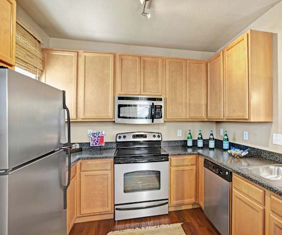 A large, modern kitchen with stainless steel appliances, kitchen utensils, dark countertops with lots of room, and large, light wooden cabinets at the Palms at Briarwood Apartment Homes. 
