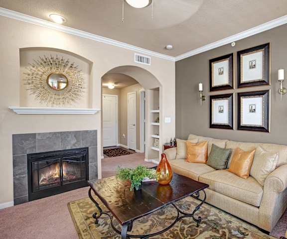 The amazing resident lounge with a cozy fireplace, a beige couch, decorations, light yellow plush chairs, a green lamp, and coffee tables at the Palms at Briarwood Apartment Homes. 