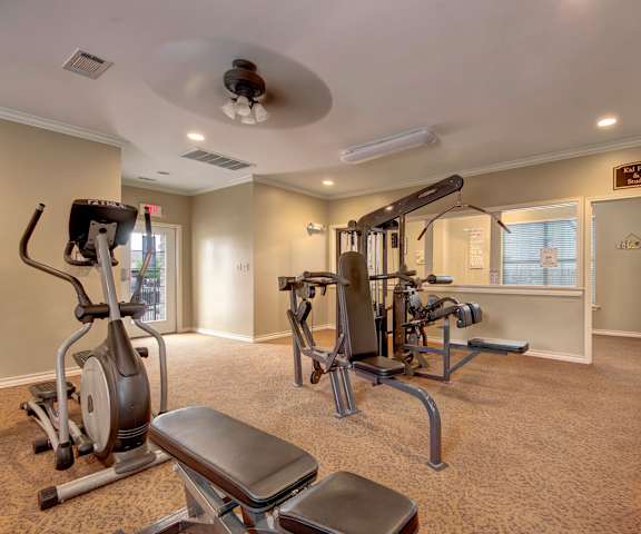 A spacious gym with cardio machines, windows, TVs, and weights at the Reserve at Abilene Apartment Homes. 