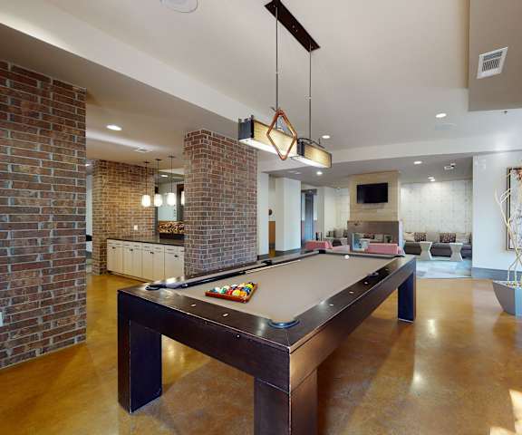 A wonderful resident lounge with tables, chairs, a kitchenette, a gray couch along the wall, and a pool table at Sorrel Fairview Apartment Homes. 