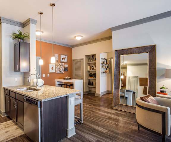 A large modern kitchen with stainless steel appliances, kitchen utensils, granite countertops with lots of room, a kitchen island with white barstools, and large wooden cabinets at Sorrel Fairview Apartment Homes. 