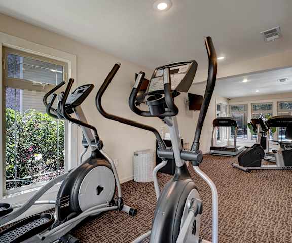 A spacious gym with cardio machines, windows, TVs, and weights at the Bradford Apartment Homes. 