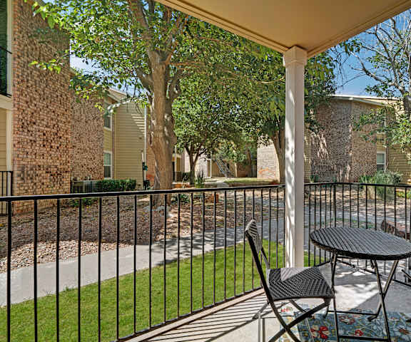 The private patio with a fenced patio, a small black table, two black chairs, a rug, and a view of the other apartment buildings and the pathways between the apartments at the Bradford Apartment Homes. 