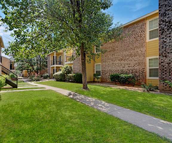 The stunning pathways surrounded by grass and trees between the yellow and brick apartment building at the Bradford Apartment Homes. 