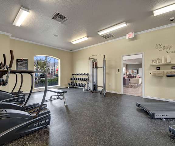 A spacious gym with cardio machines, windows, TVs, and weights at the Residence at Heritage Park Apartment Homes. 