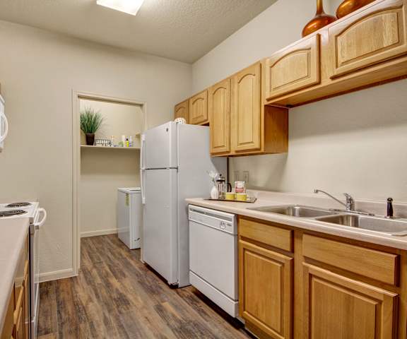 A cozy kitchen with white appliances, kitchen utensils, overhead lighting, light countertops with lots of room, and light, large wooden cabinets at the Residence at Heritage Park Apartment Homes. 